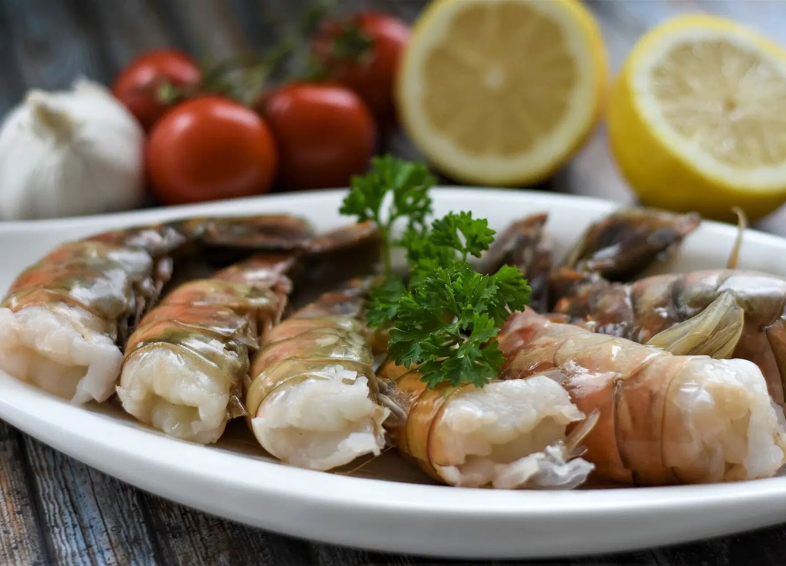 A plate of cooked shrimp garnished with parsley, alongside lemons, garlic, and tomatoes | Altamont Court, Jamaica