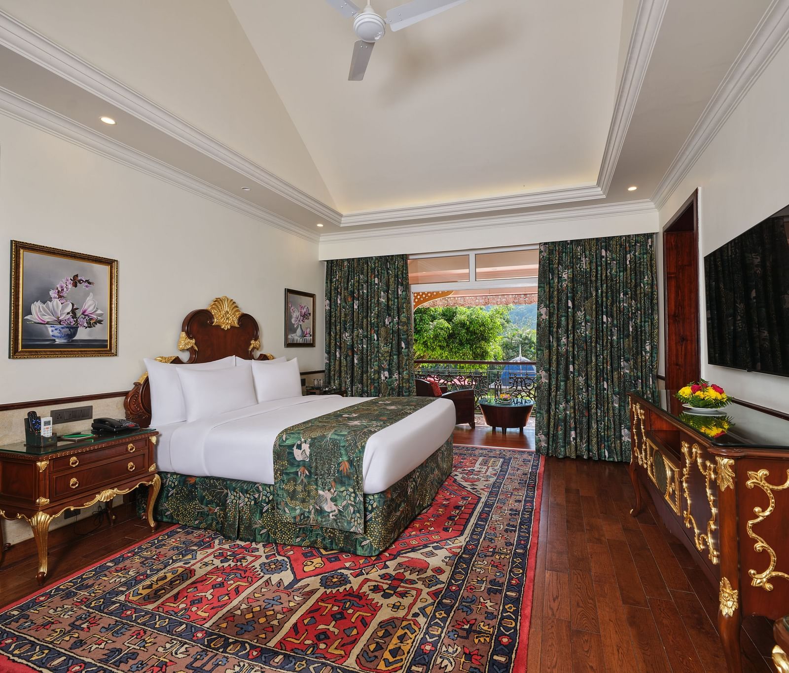 a Family Room bedroom with a large bed on a decorative rug, wooden cabinet, TV, artworks, and a window overlooking greenery 