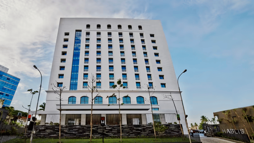 Daytime facade view of Hablis Hotel in Chennai with street lights in front of it and blue sky in the background. One of the best Corporate Team Outing Places in Chennai.