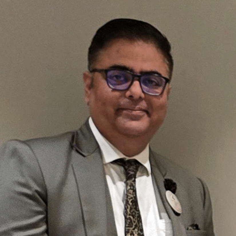 A head-and-shoulders portrait of a man with short dark hair and glasses, wearing a gray suit jacket, a striped tie, and a light-colored shirt. He is looking directly at the camera.