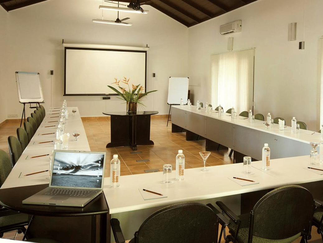 Conference Hall in Bandipur at The serai Bandipur with a U-shaped table and a projector screen under warm lighting
