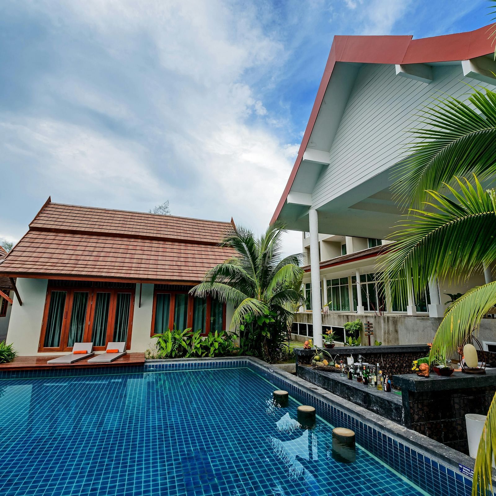 facade image of a resort overlooking a clear blue swimming pool surrounded by green plants in the corner