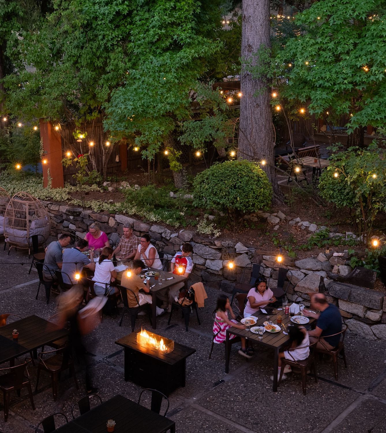 Outdoor evening dining area with guests enjoying a meal under string lights at The Groveland Hotel.