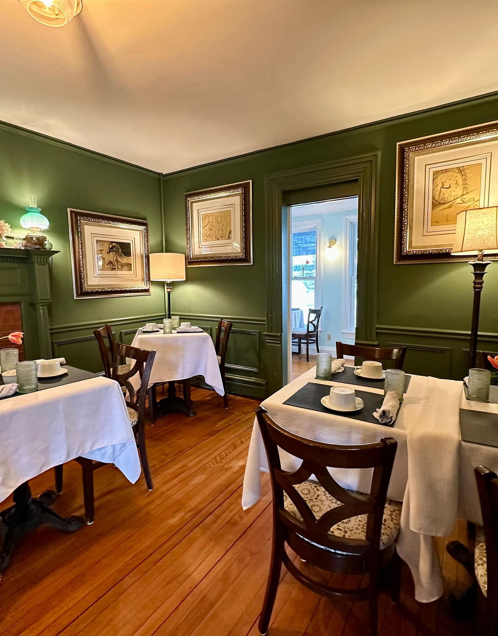 A dining room at Hartstone Inn featuring green walls, white tablecloths, and framed artwork