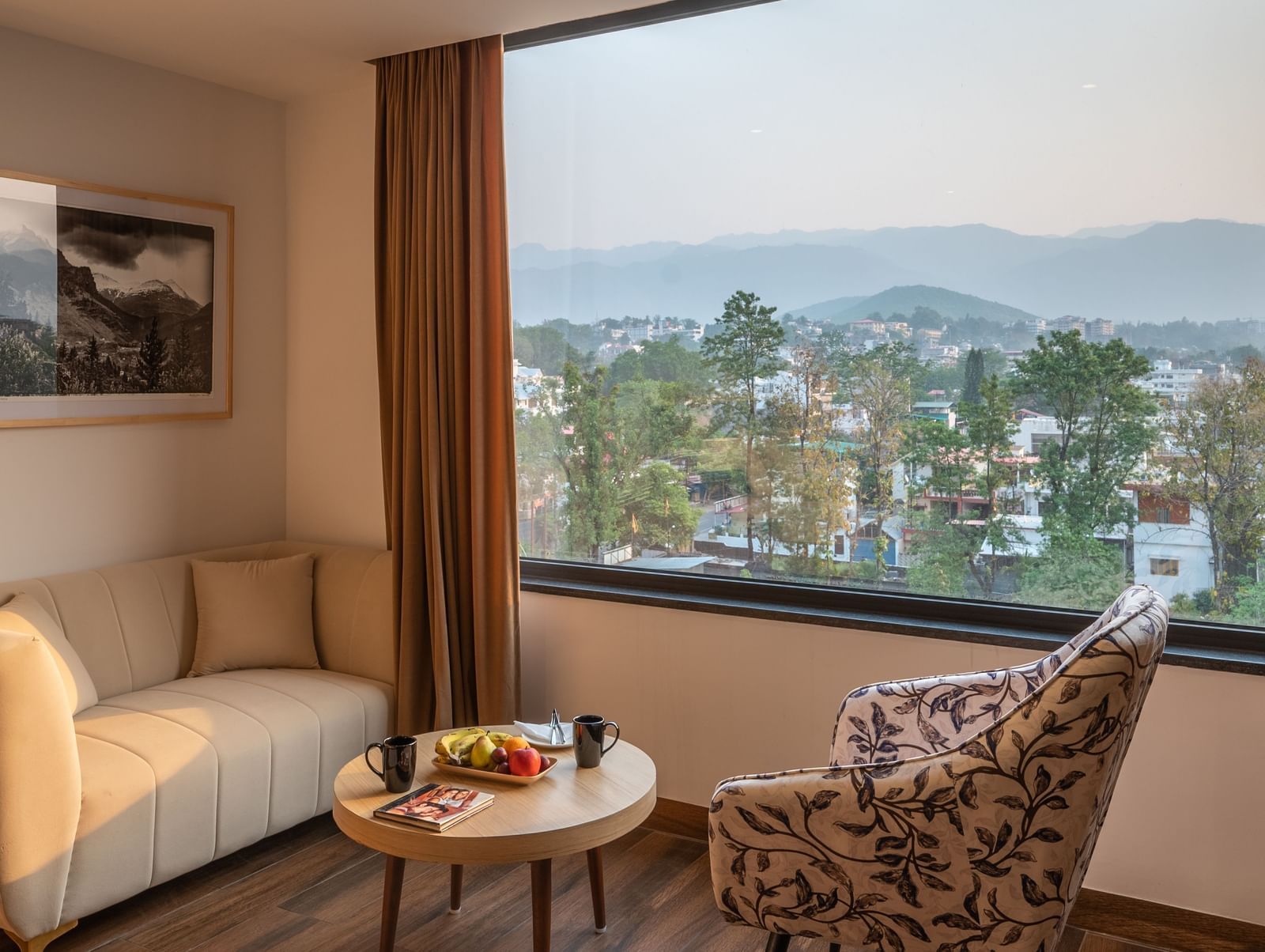 Living area of the lavish suites in Dehradun at Vishranti Hotel featuring a large window, a sofa, chair and a round table.