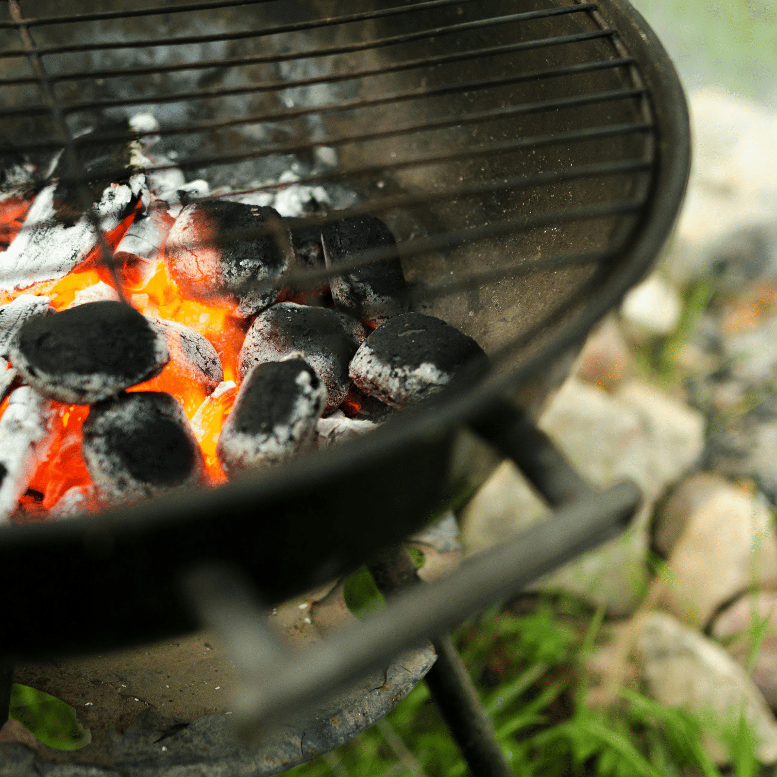 Close up of an active charcoal grill placed outdoors on top of rocks.