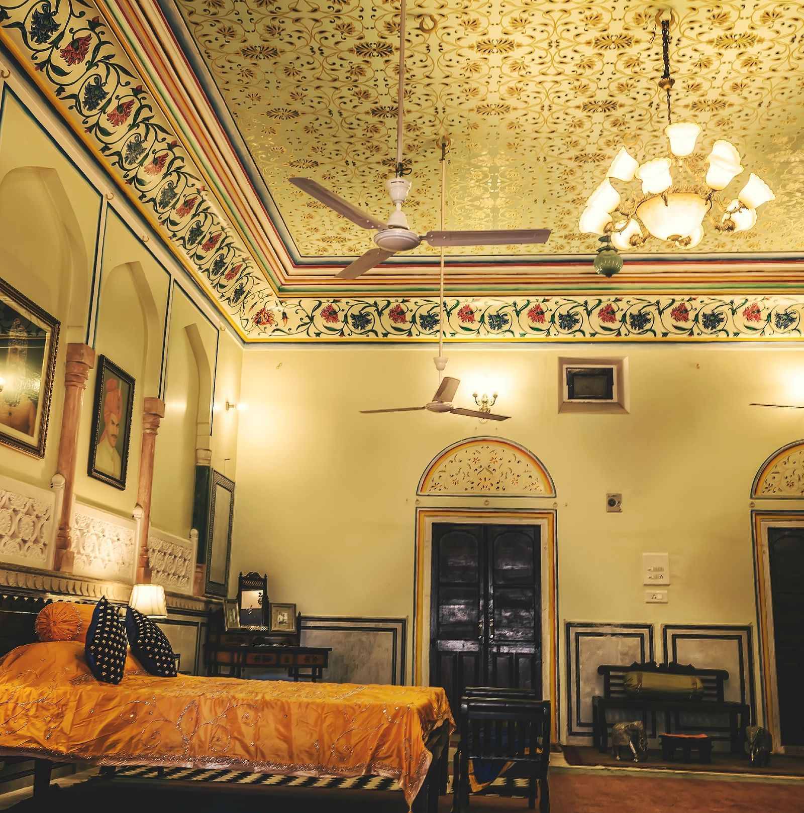 A room at The Umaid Vilas, Jaipur with a double bed, paintings hanging on the wall and a chandelier hanging from the ceiling