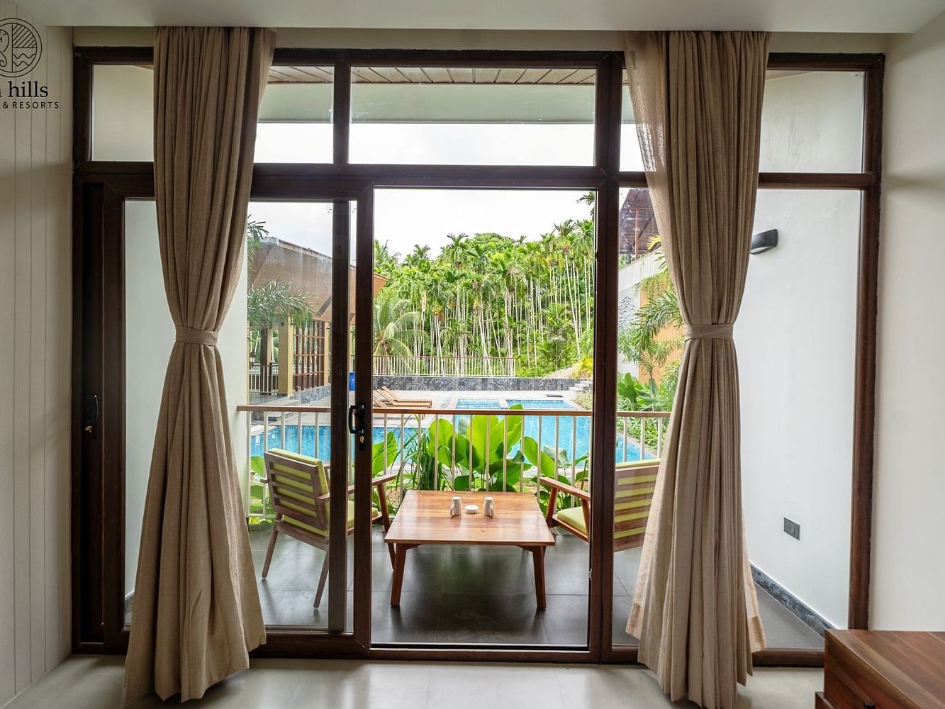 Room with large glass windows offering a scenic view of the pool, accompanied by comfortable wooden furniture - Sea Hills Resort, Swaraj Dweep (Havelock)