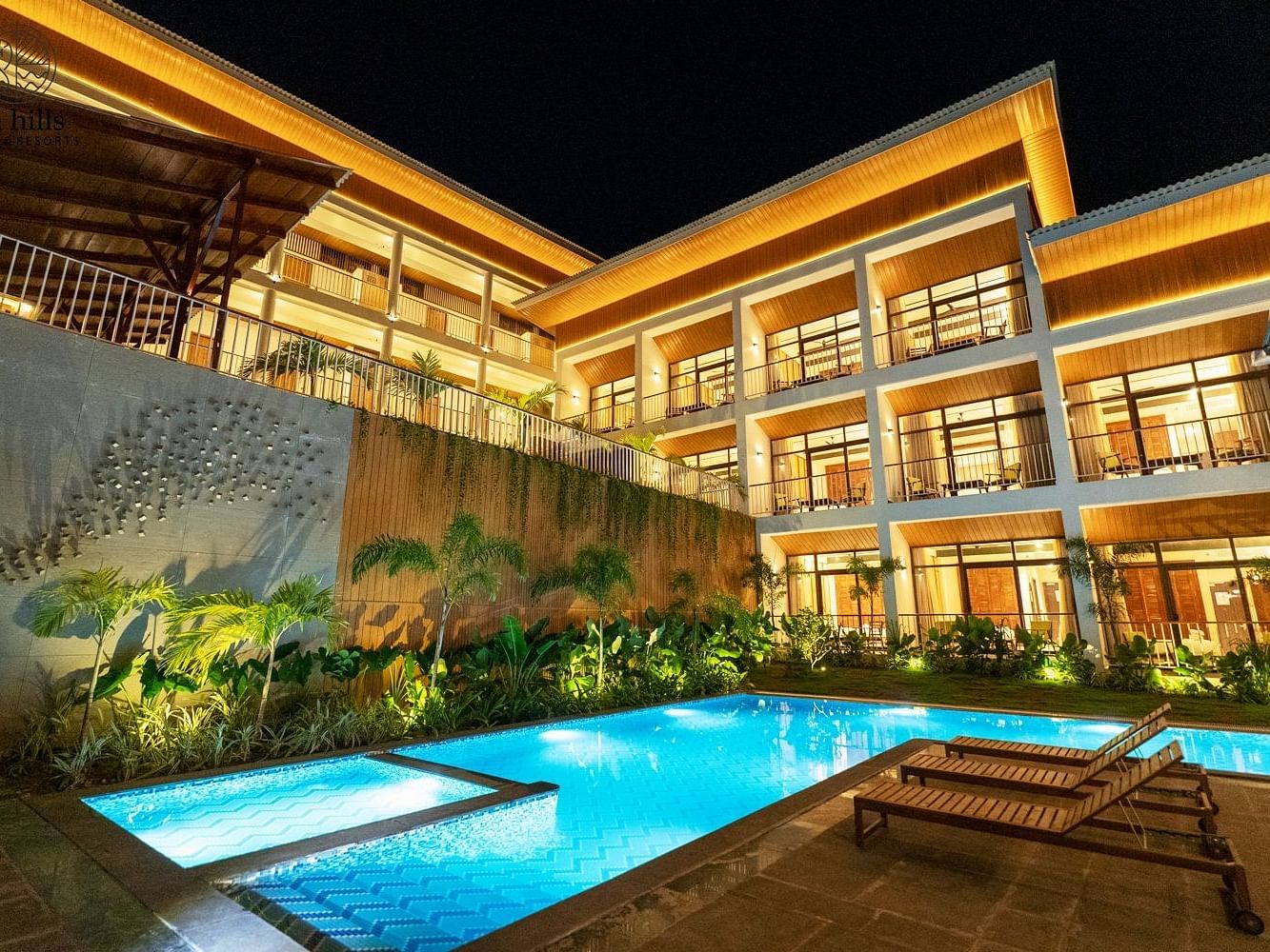 An exterior night view of a luxurious hotel building with a brightly lit swimming pool and lush landscaping. - Sea Hills Resort, Swaraj Dweep (Havelock)