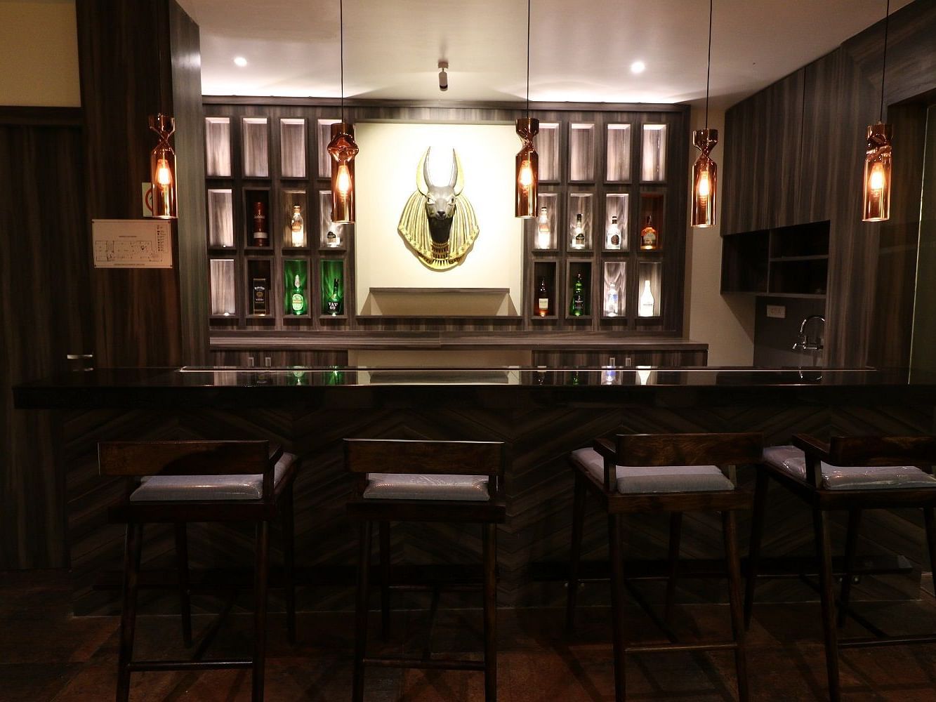 A dimly lit, sophisticated bar area with a long counter, bar stools, and bottles displayed on shelves - Sea Hills Hotels, Sri Vijayapuram (Port Blair)