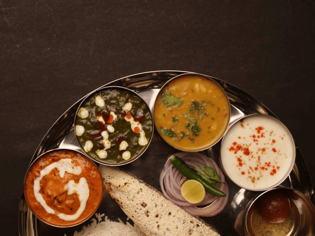  A close-up of a round plate holding a traditional Indian thali meal, including various curries, flatbreads, and rice.