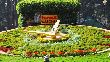 A clock-like statue in a lush green garden.