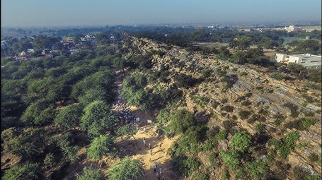 Aerial view of a lush green, tree-covered landscape with some open ground patches.