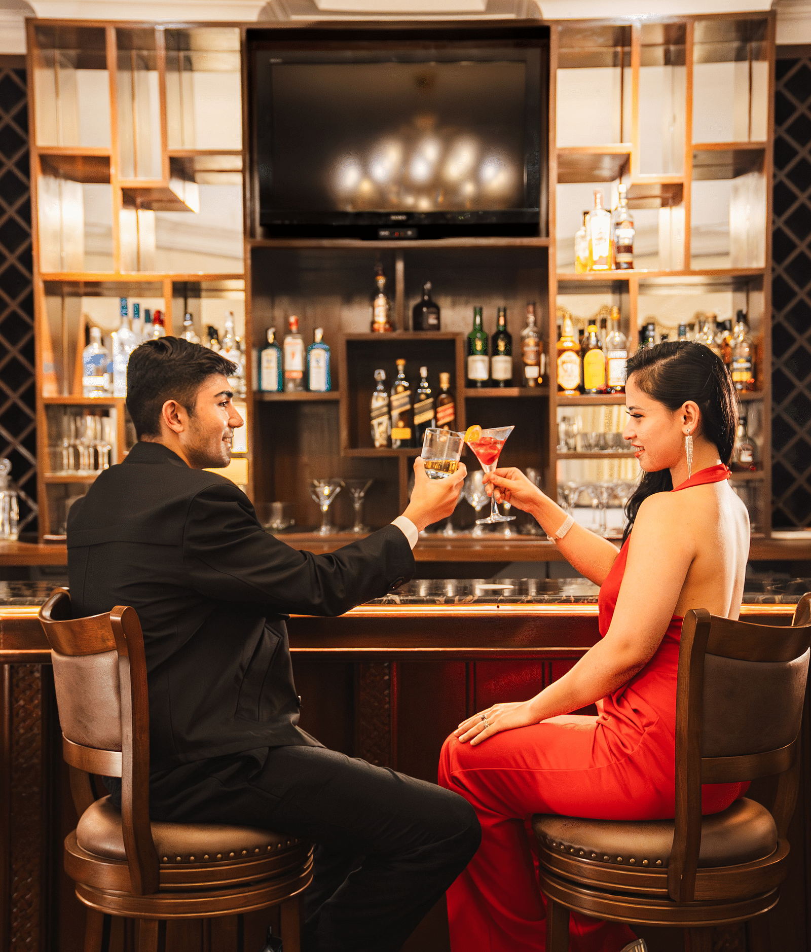 A picture of two people enjoying drinks at an elegant bar, with a warm and sophisticated ambiance enhanced by classic décor and seating