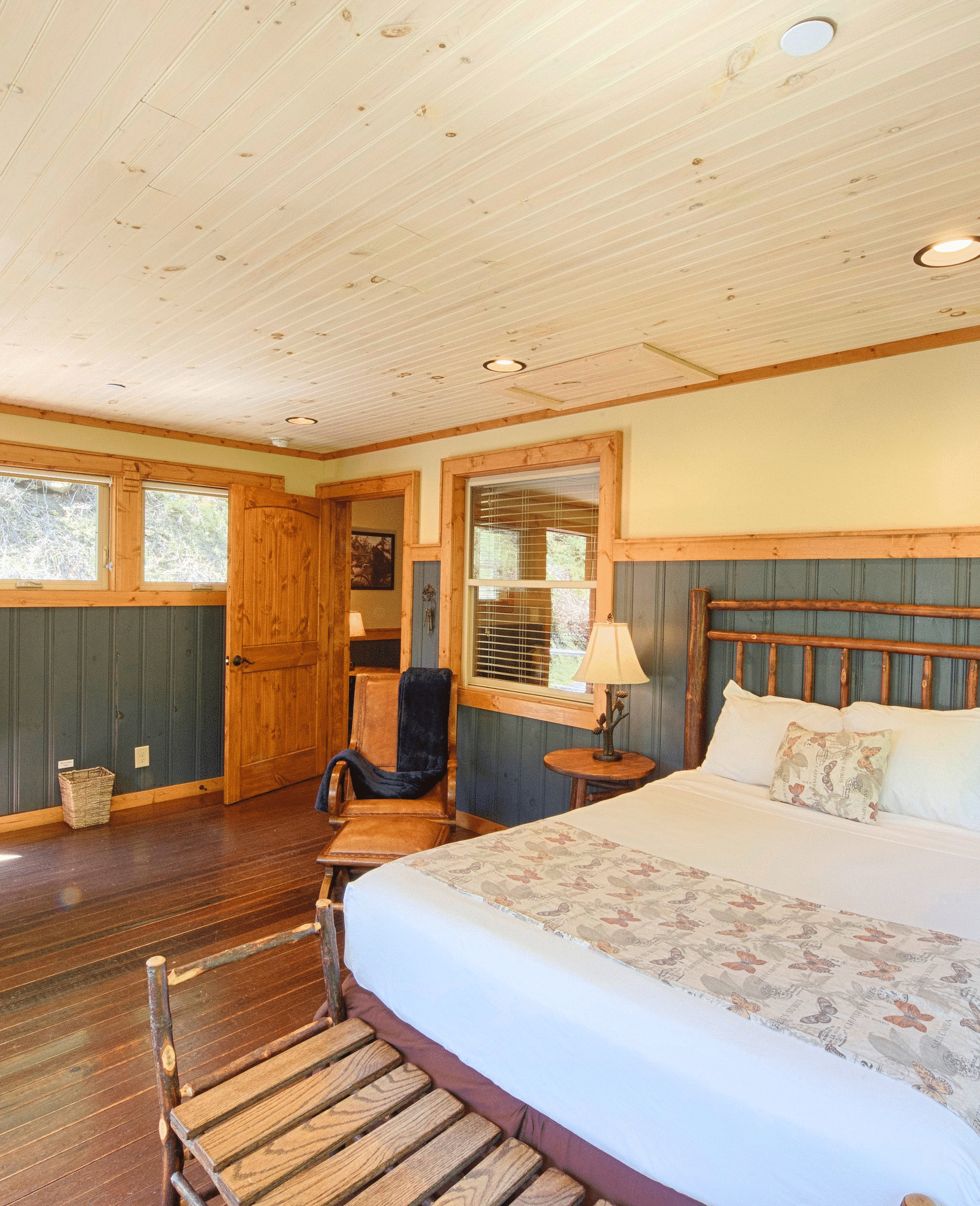front view image of a bedroom with vibrant interiors and wooden flooring featuring a double bed with a vintage tall lamp besides it -Historic Tapoco Lodge