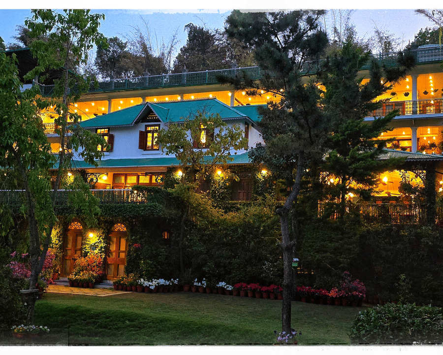 Twilight view of Shaheen Bagh-Dehradun, a luxury boutique resort and spa, with warm lights illuminating its green-trimmed architecture and lush gardens.