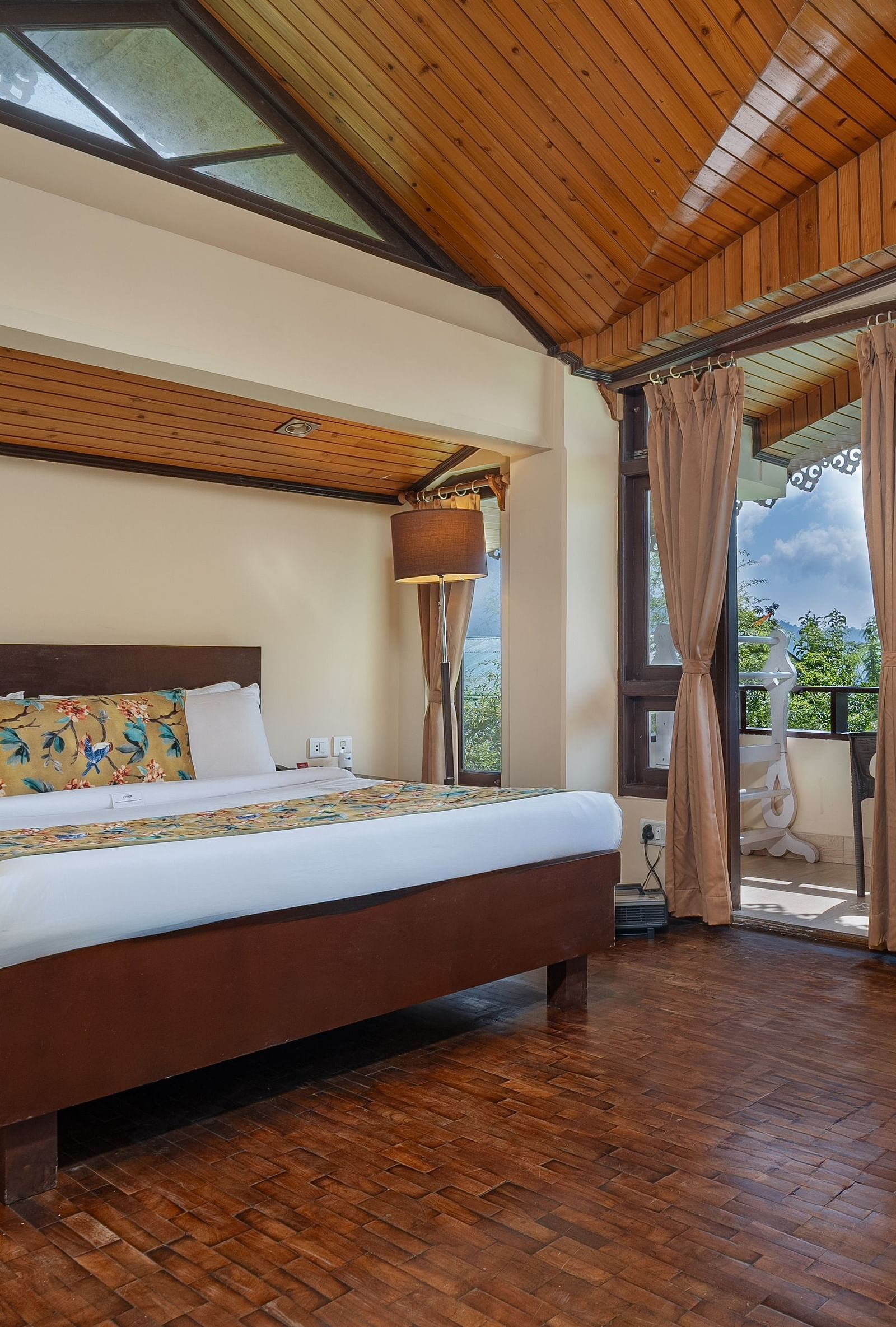 Deluxe room featuring a private balcony, spacious bed, wooden table with cushioned seating, and warm lighting at Summit Norling Resort & Spa, Gangtok