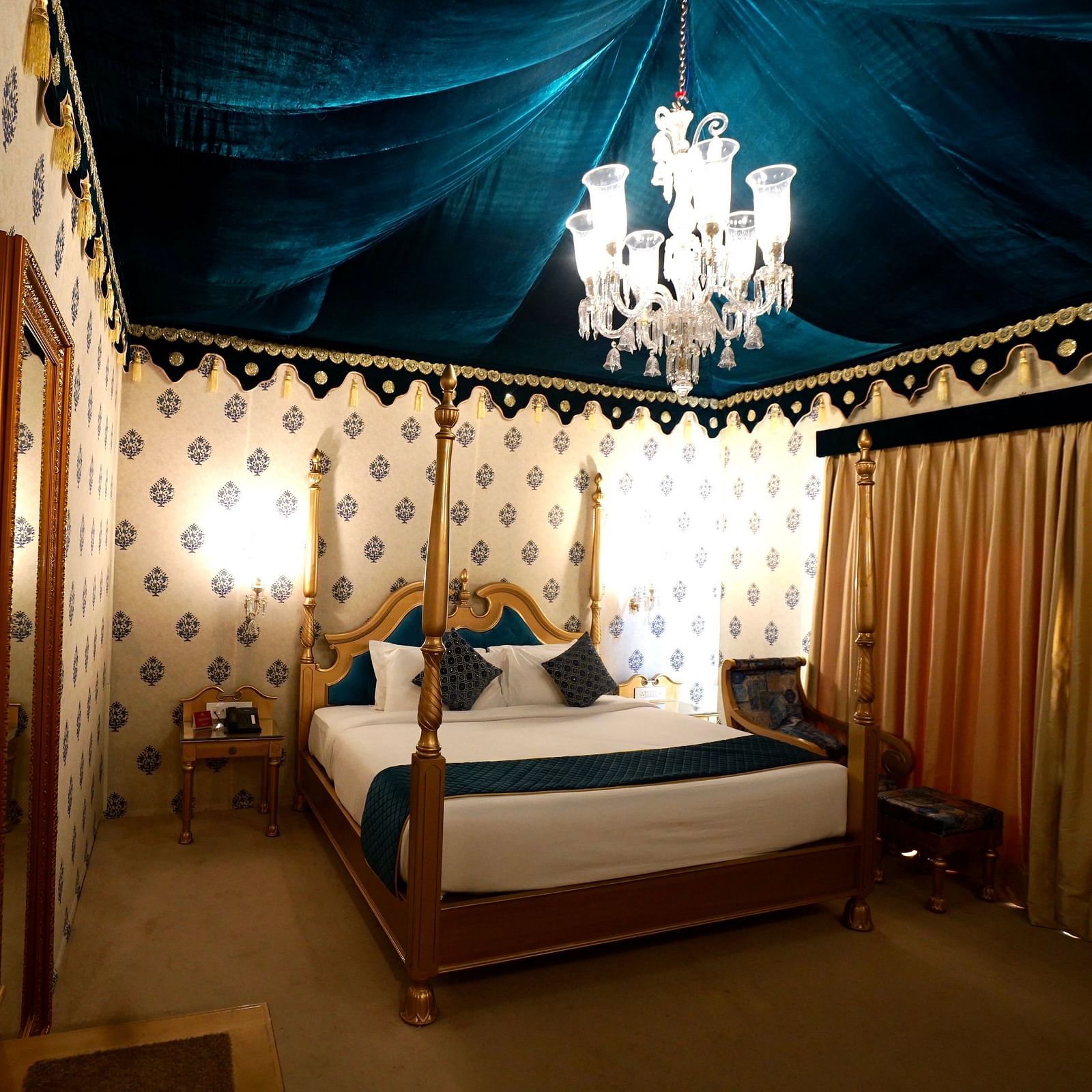 Image of a room with a bed, a mirror on the side and a chandelier hanging from the ceiling.