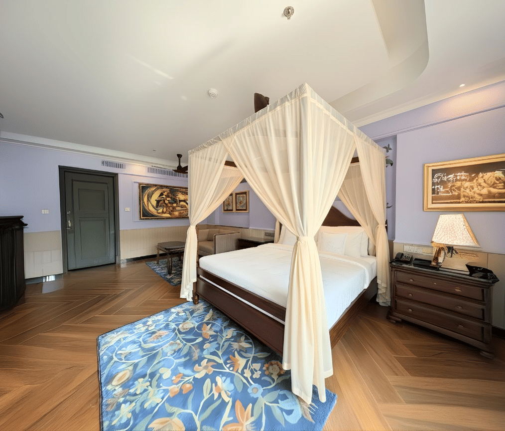 A room with a four-poster bed, draped curtains, artwork on the walls, wooden flooring, abstract blue coloured rug, and soft lighting at MAYFAIR Bay Resort, Paradeep.