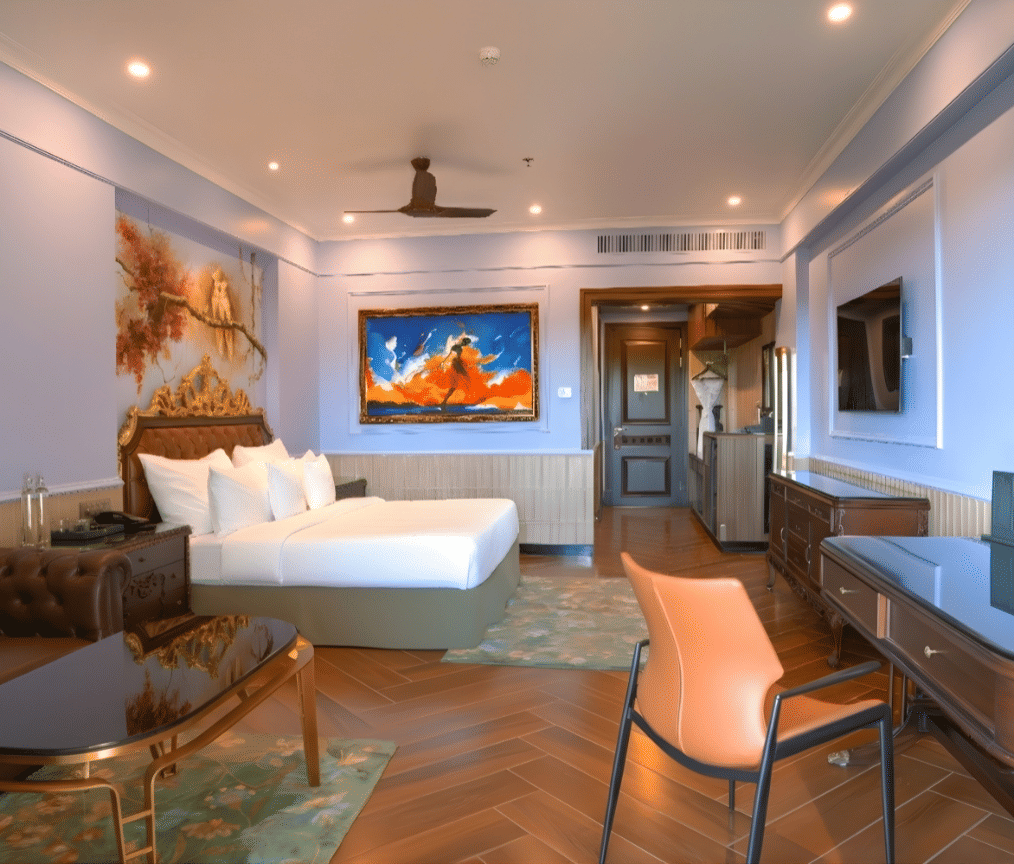 An elegant room featuring a white king size bed, seating area with patterned furniture, a work desk and a chair, a wall mural and an abstract landscape painting above the headboard at MAYFAIR Bay Resort, Paradeep.