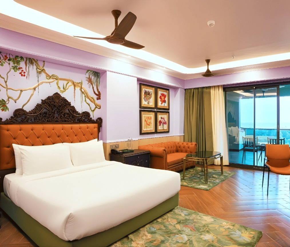 A brightly designed room featuring a king size bed with upholstered headboard, floral mural, lounge chairs, balcony access and wooden flooring at MAYFAIR Bay Resort, Paradeep.