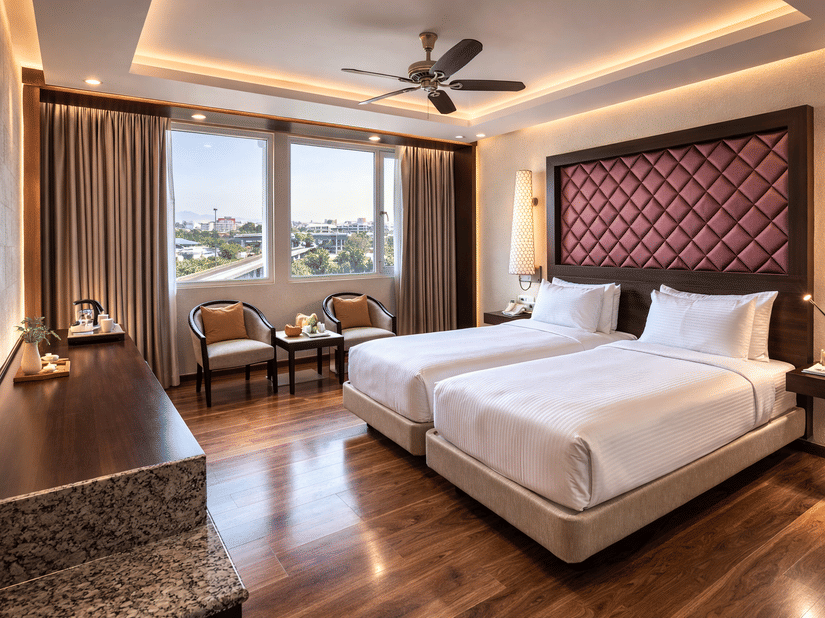 A room at Clarks Avadh, Lucknow, featuring twin beds, spreads, pillows, a television, and large windows.
