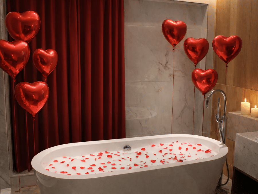 Valentine’s Day romantic bath setup at Pride Hotels Group with rose petals, heart balloons, candles and luxury bathtub.
