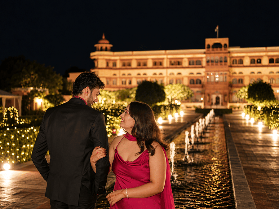 Couple standing in an illuminated night courtyard beside a central water fountain feature at Umaid Palace.