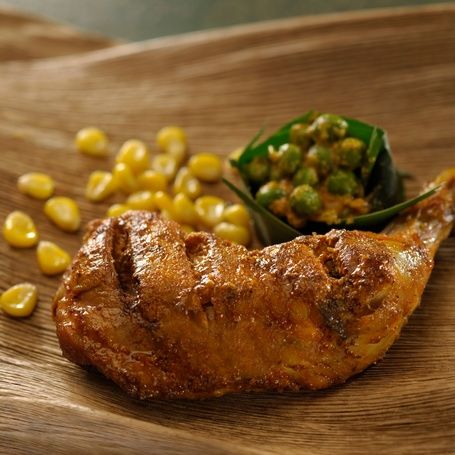 Roasted chicken leg with corn and peas on a plate.