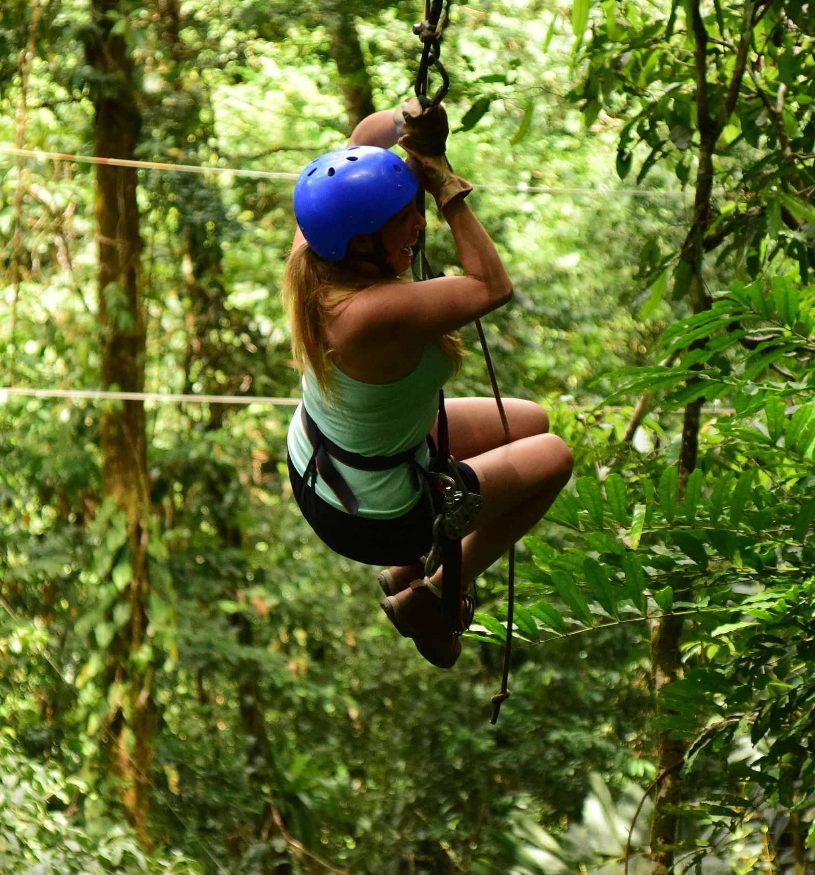 A person wearing a helmet and harness ziplining through a dense forest.