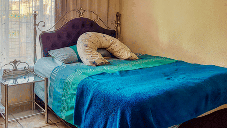 A bedroom featuring a double bed with sheets spread over it with beige curtains covering the window behind it.