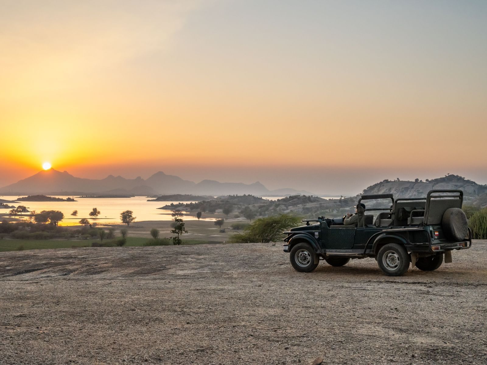 A jeep parked before a mountain with view of the sunrise at KURJA Jawai.
