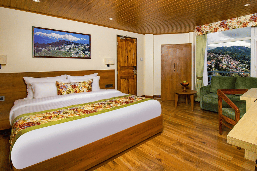 Our room featuring a balcony, warm wooden interiors, a king size bed, seating area, and spacious layout | Mount Lungta - A Darjeeling Hotel with Balcony
