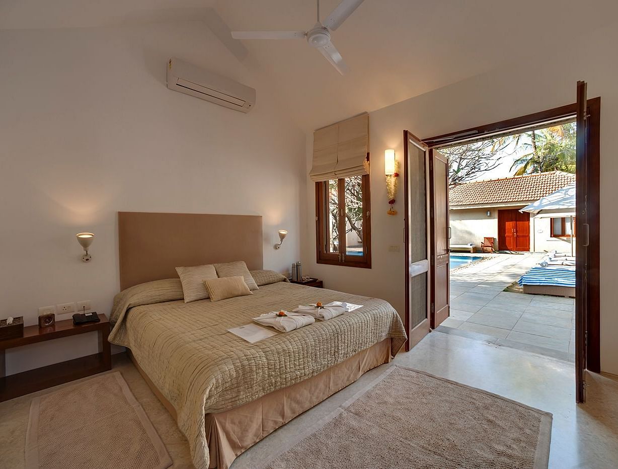 Neatly arranged bed with cushions and a view of the pool outside - Shreyas Retreat