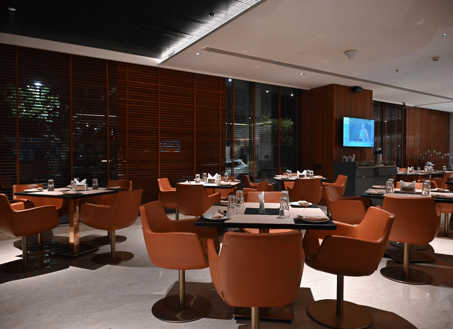 A contemporary dining area with round tables and orange chairs set against a warm, wooden backdrop.