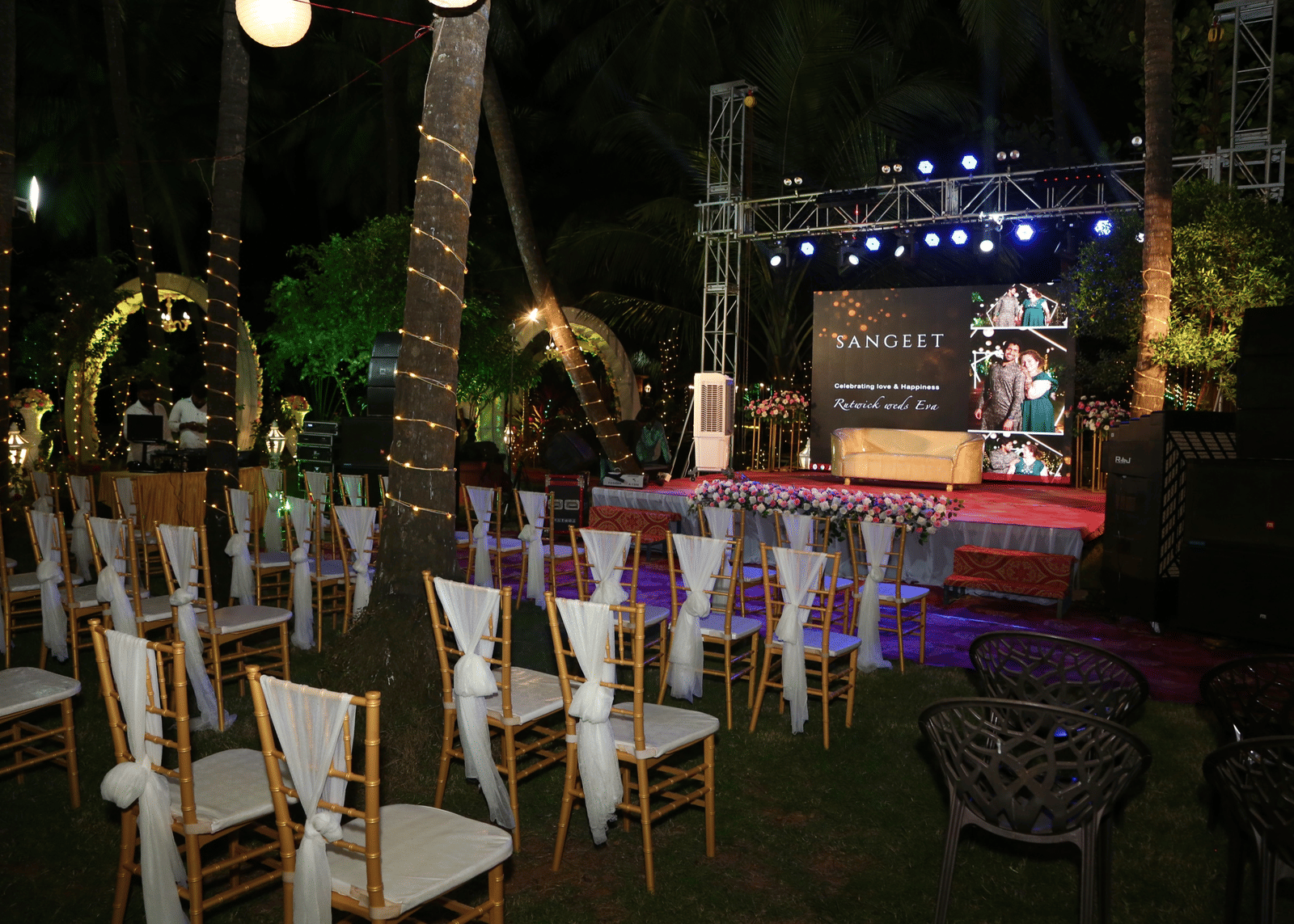 Outdoor seating with white chairs arranged before decorated stage at Paradise Lagoon Resort, Udupi.