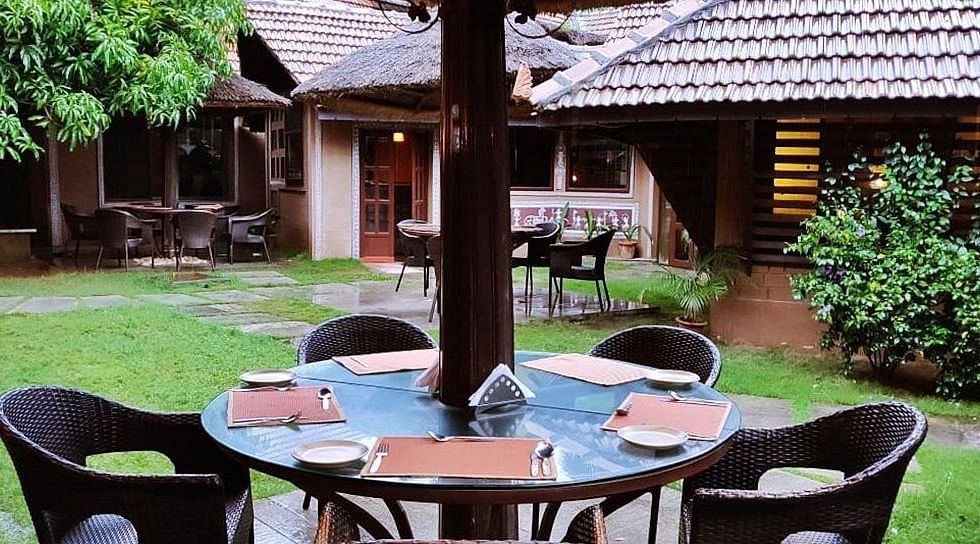 image of an outdoor dining area at hoysala village resort with four chairs surrounding a round glass top table.