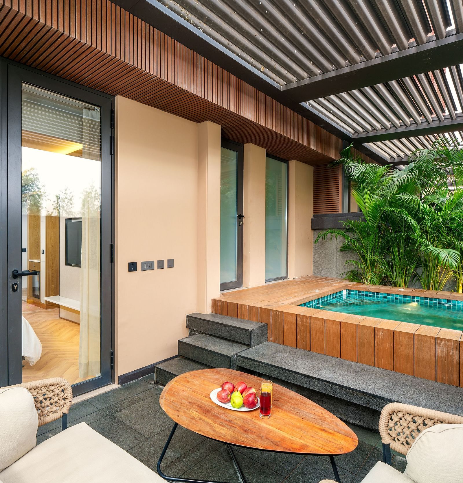 A luxurious villa at Nirvana Luxury Hotel, Ludhiana, features a private plunge pool surrounded by lush greenery, a cosy outdoor seating area with a wooden table, and direct access to the villa's interior.