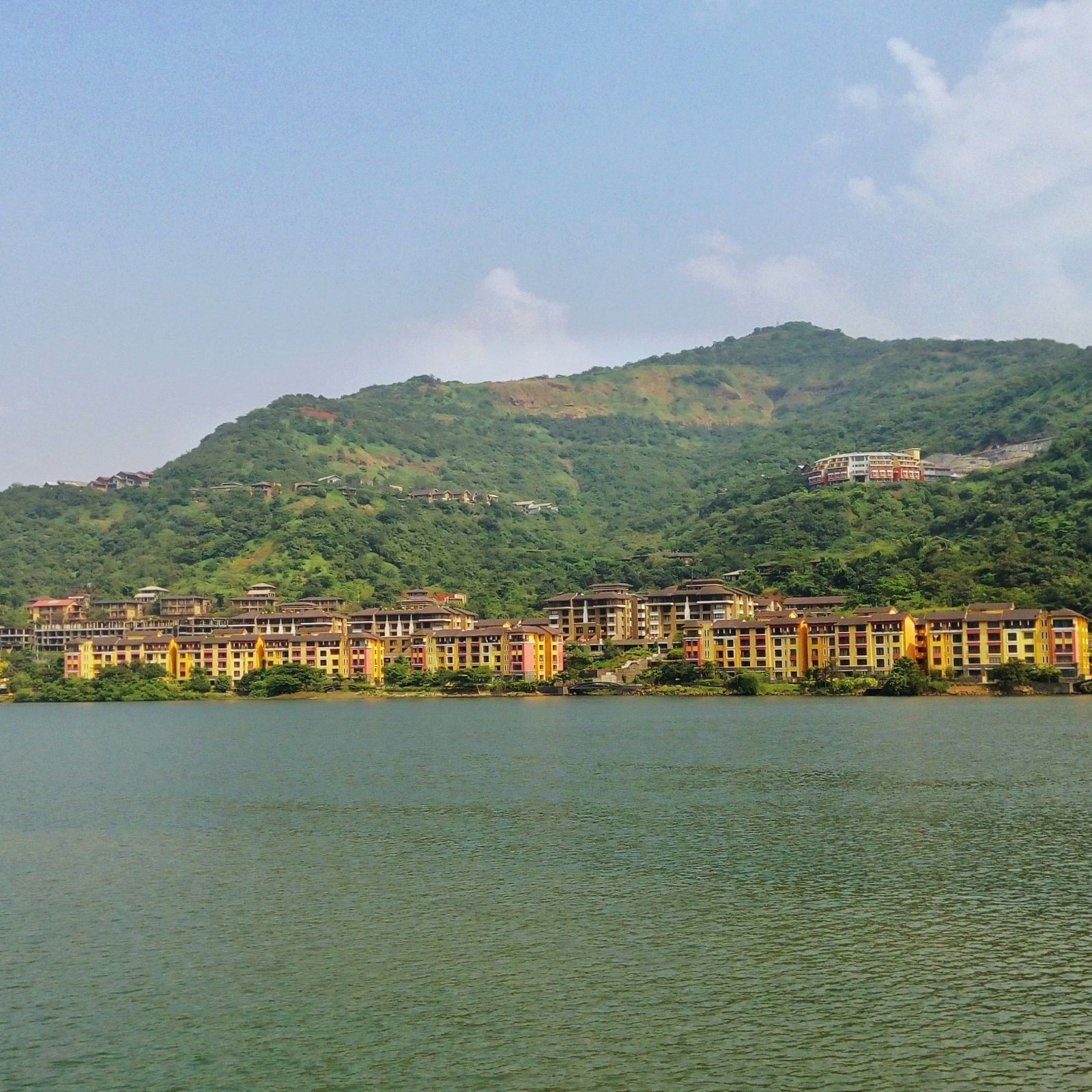Calm waters reflecting green hills and scattered houses along the shoreline under a clear sky.