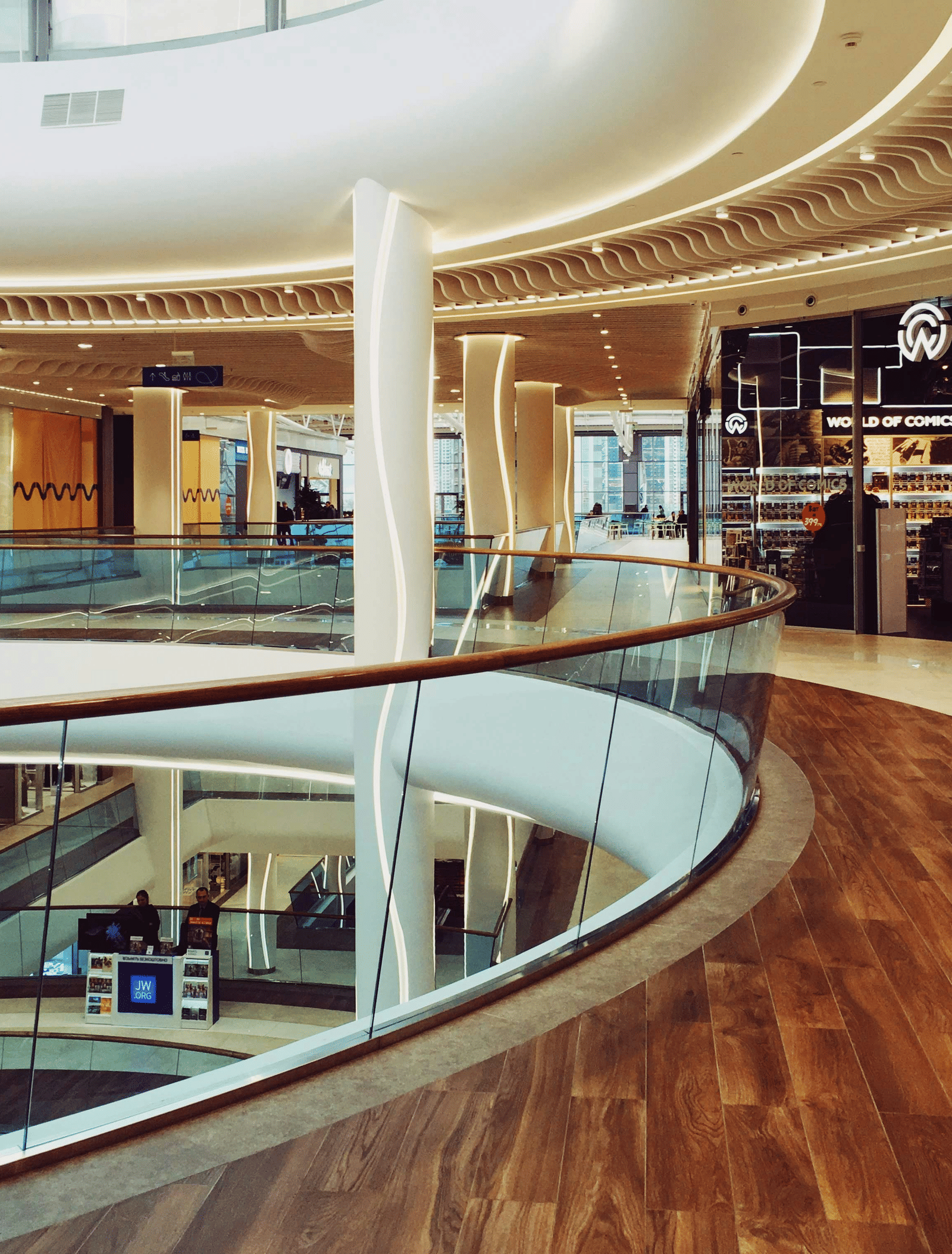 A curved indoor balcony walkway inside a shopping centre overlooking lower floors.