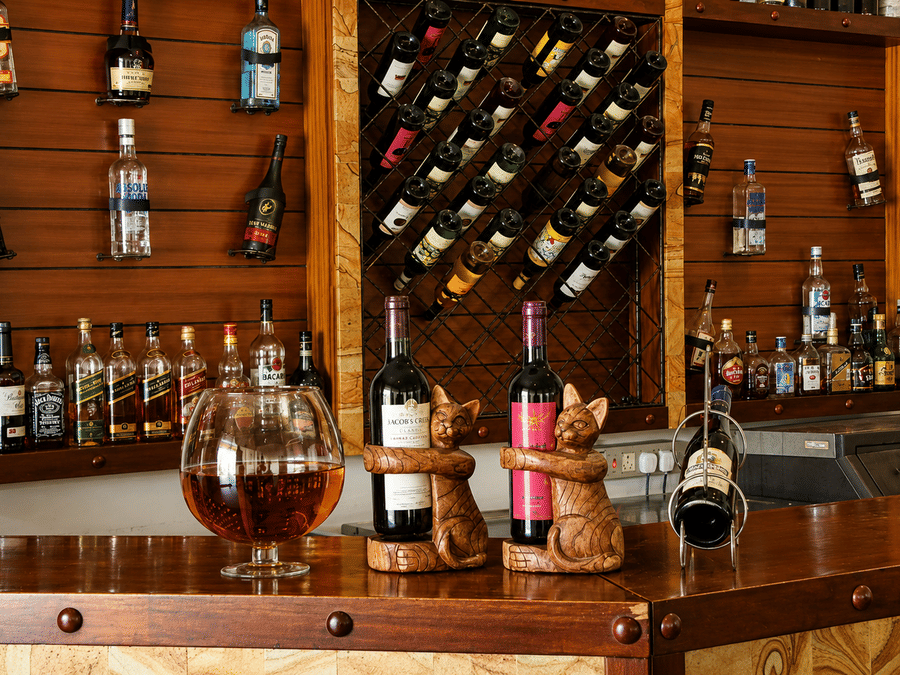 Paanam - The Bar shelf stocked with a curated selection of wines and spirits, set against warm wooden shelving and lighting