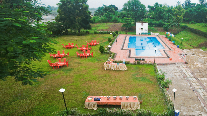 Full view of the Poolside Party Lawn featuring chairs and tables set on the lawn by the pool under a cloudy sky - VITS Kamats Resort, Silvassa