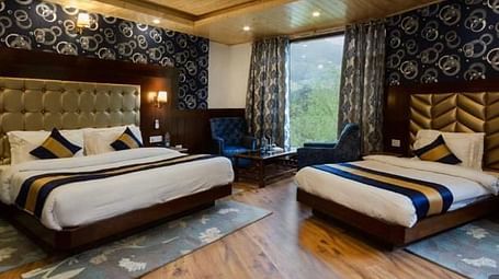 A spacious, well-lit hotel room at La Serene Valley by DLS Hotels in Manali, India. The room features two beds, a sitting area, and large windows offering natural light and views of the surrounding mountains | DLS La Serene Manali
