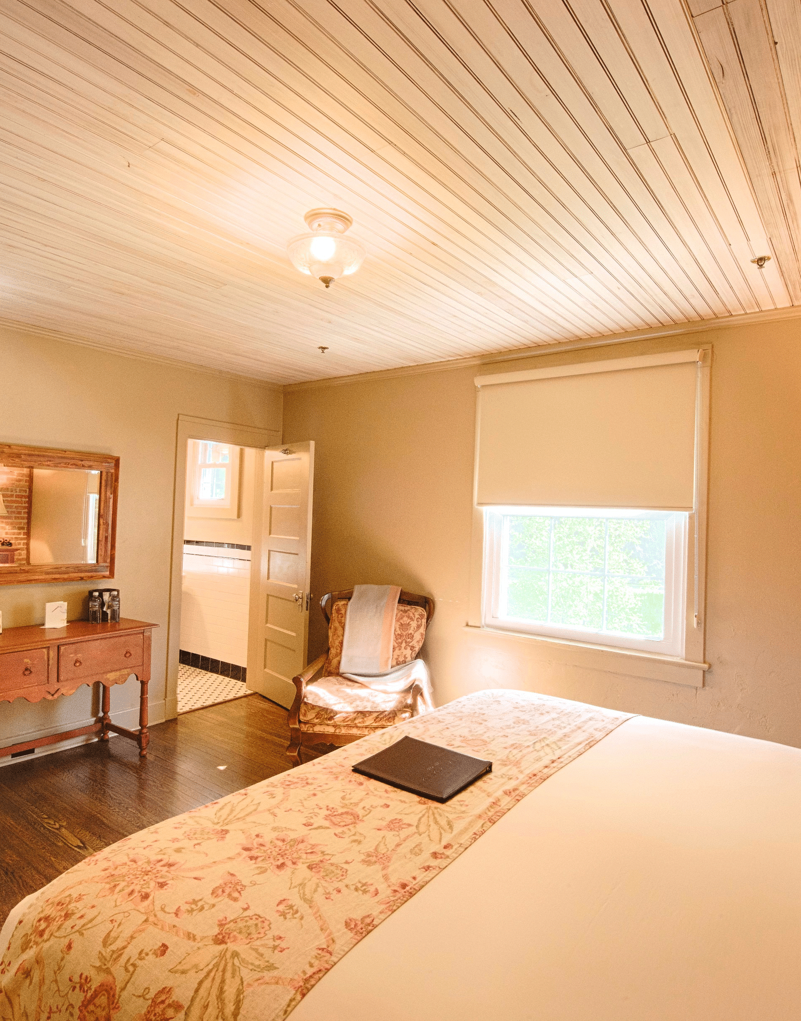 side view image of a bedroom highlighting the smooth sheets spread over the double bed along with a wooden table opposite to it - Historic Tapoco Lodge 