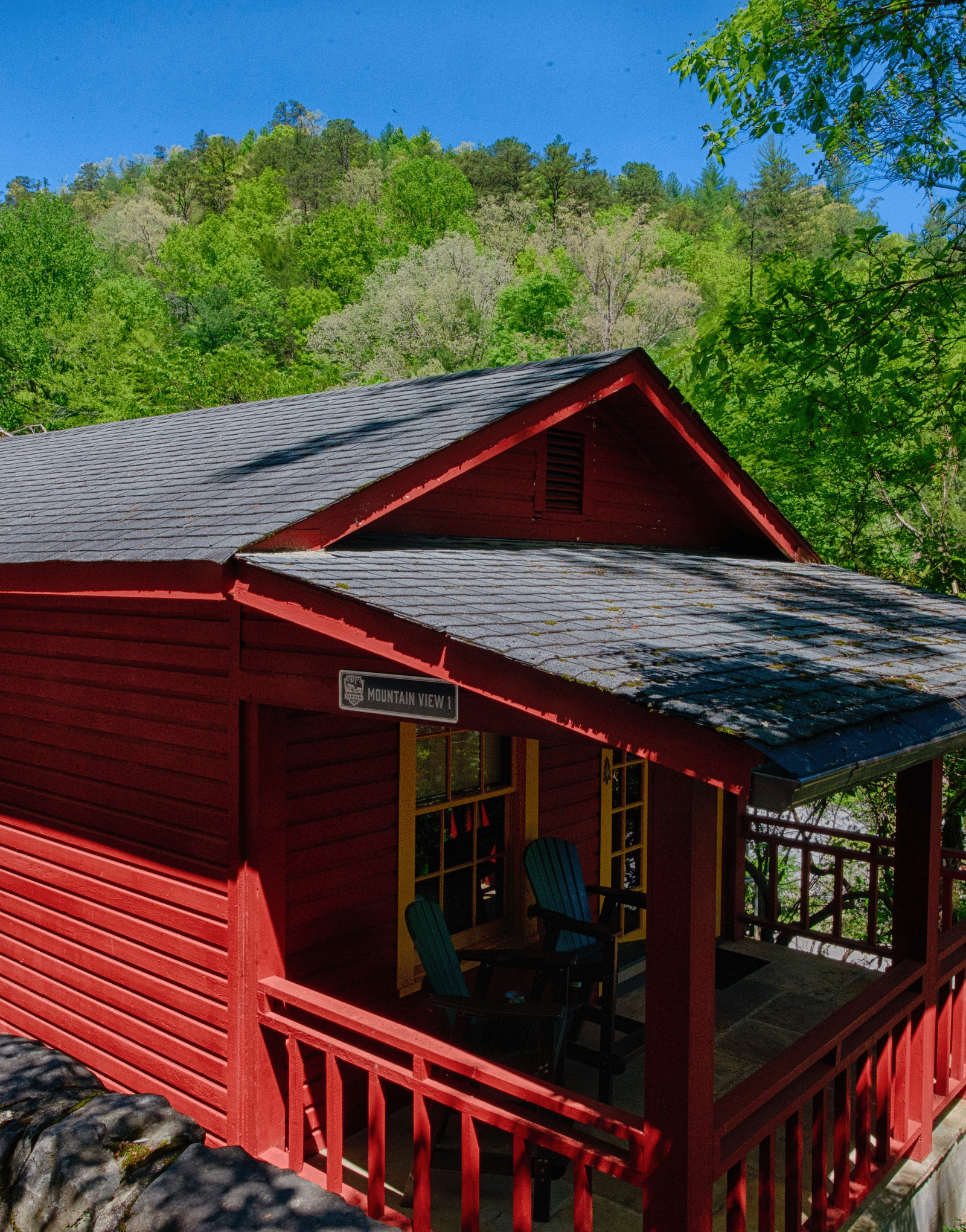 a bright facade image of a cabin win bright red colored exterior with lush green mountains in the background - Historic Tapoco Lodge