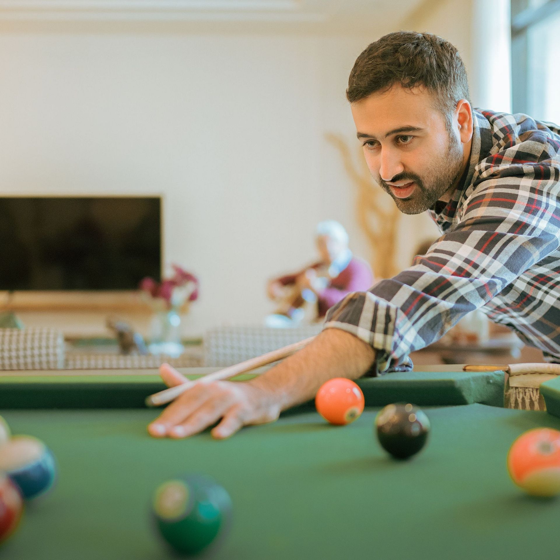 Guest playing a game of pool inside Karma Chalets, with a green pool table and indoor seating area in the background.