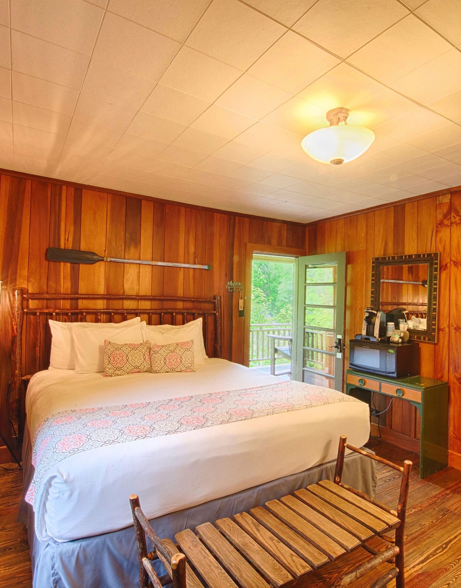 front view image of a cozy double bed in a room with wooden walls and flooring with a small chandelier - Historic Tapoco Lodge