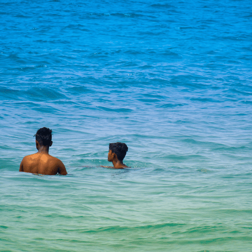 A zoomed in view of two people bathing in the Arabian Sea next to Colva Beach, one of the top 10 beaches in South Goa, in blue-green coloured waterbody.