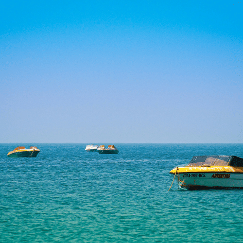 Numerous boats on the Arabian Sea next to Colva Beach with blue-green waterbody and blue sky seen.