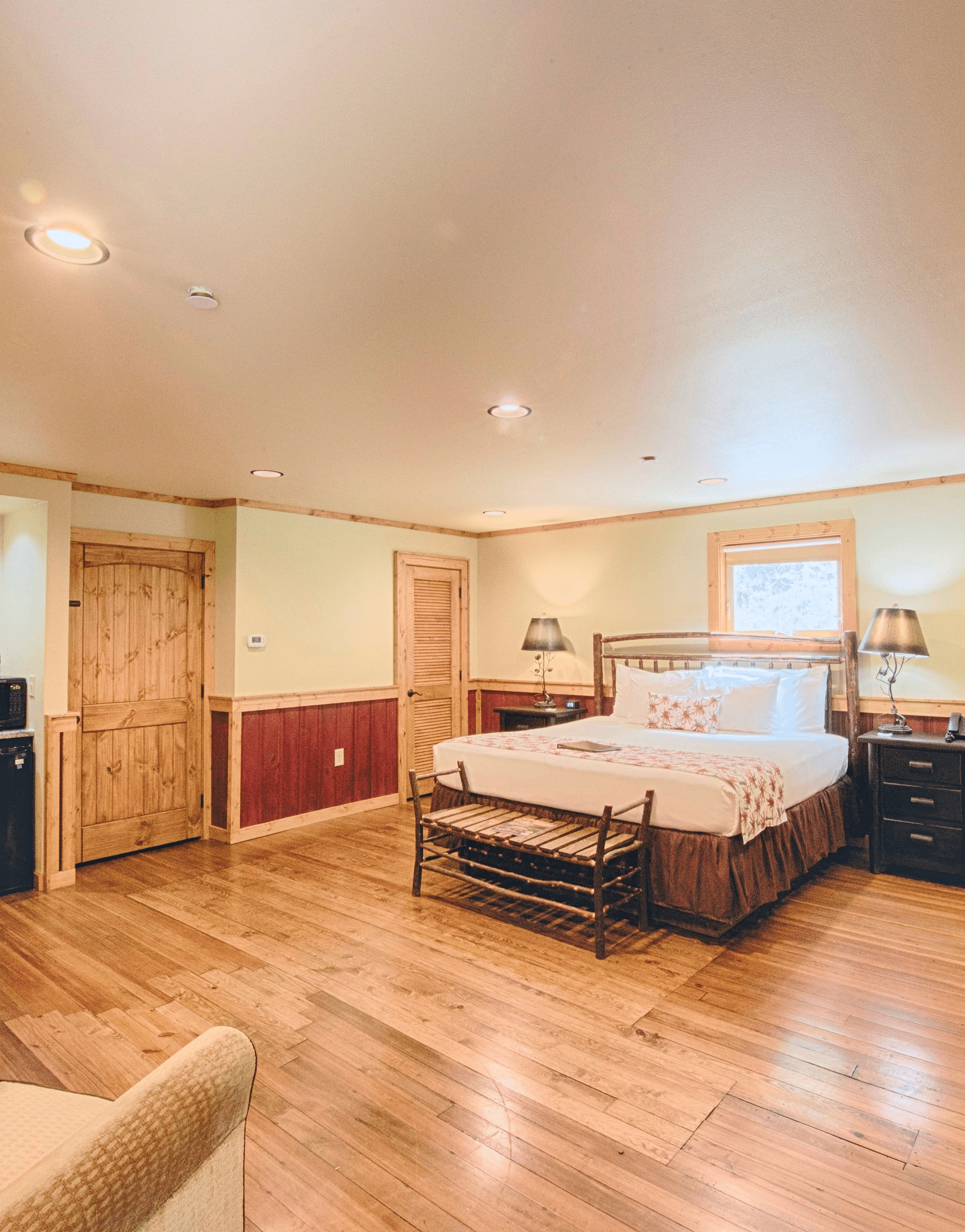 corner view image of a bedroom featuring a plush double bed in the middle and a seating area opposite to it - Historic Tapoco Lodge